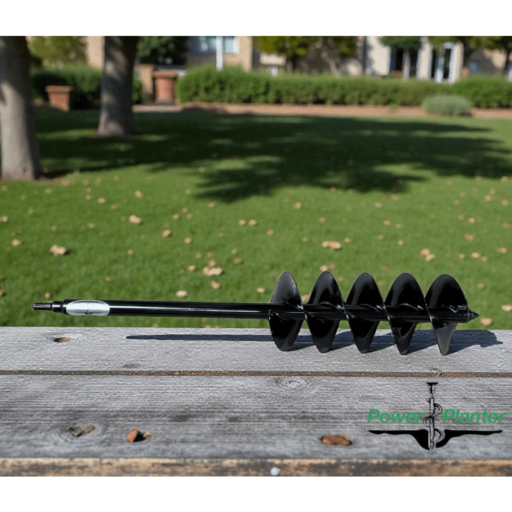 Black 5" auger on weathered wooden board, with a blurred green lawn and trees in the background.