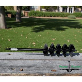 Black 5" auger on weathered wooden board, with a blurred green lawn and trees in the background. 