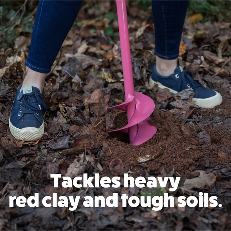 Person using a pink gardening tool to break up soil in a garden bed.